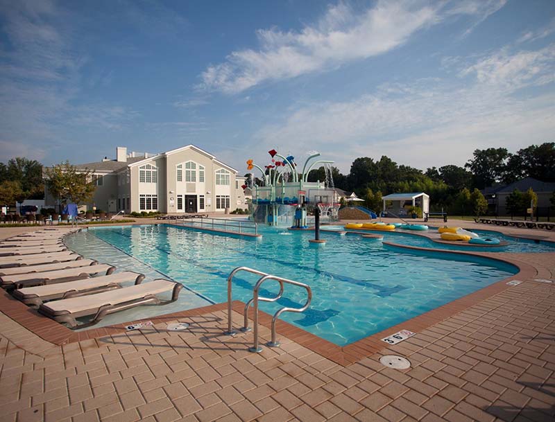 A large swimming pool with a water play feature and lounge chairs lining the edge, and the resort buildings visible in the background.