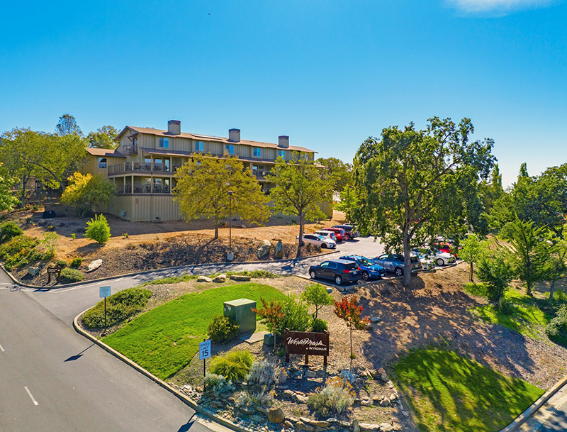 WorldMark Angels Camp’s multi-story lodge buildings and parking area, nestled on a landscaped hillside with lush green trees.