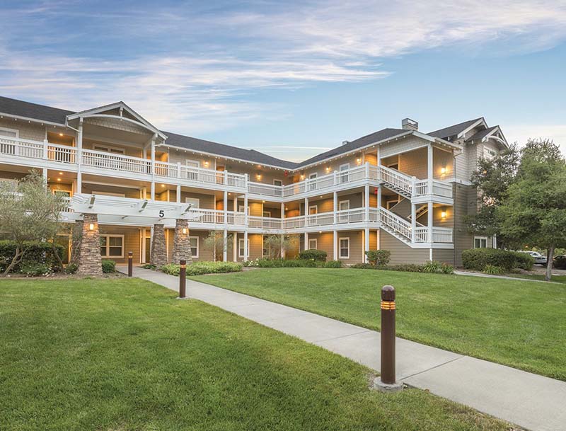 The illuminated exterior of a resort building at sunset, with a lush grass lawn and a pathway in the foreground.