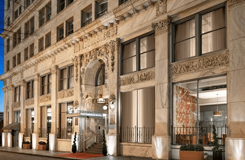 Exterior of The Candler Hotel in Atlanta with intricate decorations, many windows, and small shrubs.
