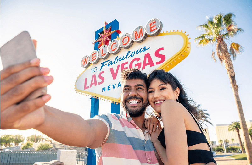 A happy couple poses for a selfie in front of the iconic Las Vegas sign.