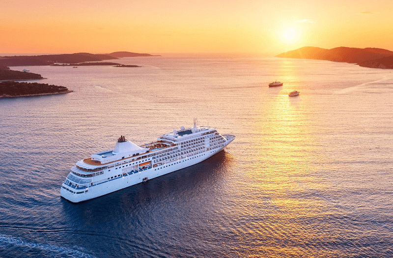 A cruise ship gliding smoothly through the ocean waters during sunset.