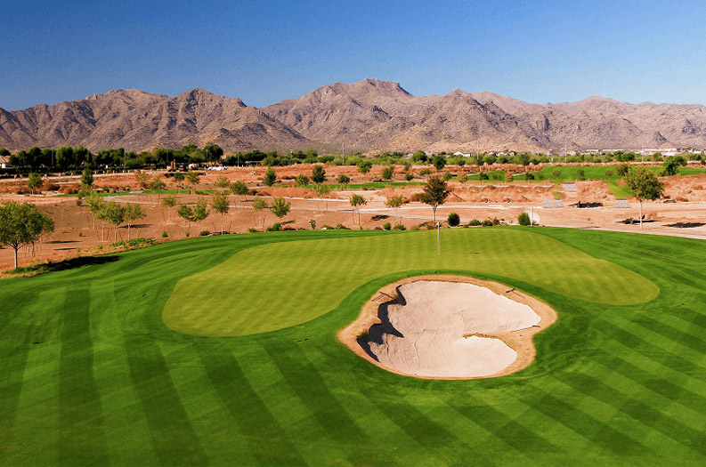 Scenic golf course featuring a sandy bunker and majestic mountains in the distance.