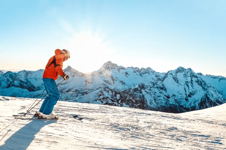 A skier on a snowy mountain, surrounded by pristine white slopes and a clear blue sky.
