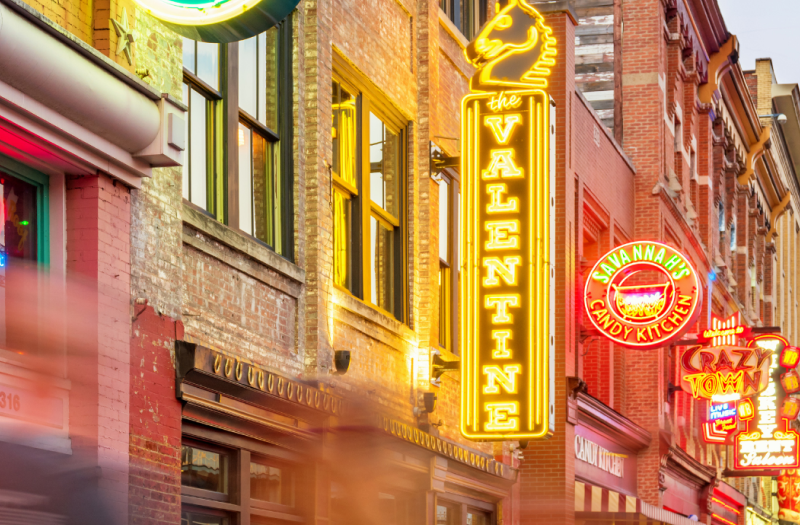 Neon-lit pubs and venues along Broadway in downtown Nashville in the early evening.