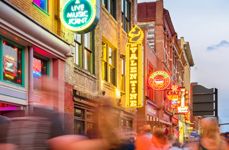 A lively Nashville street scene featuring neon signs and crowds of people walking, showcasing the city's energetic vibe.