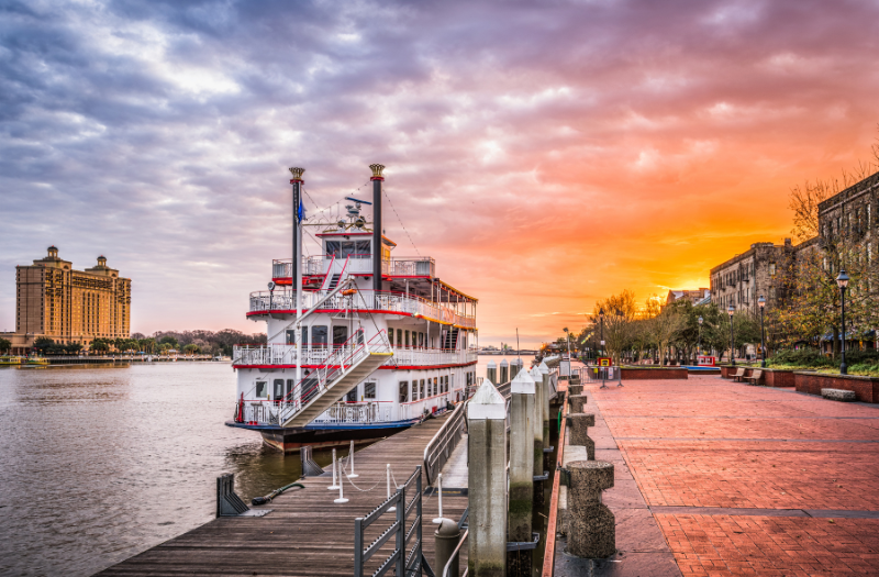 A riverboat docked in the water at Savannah, GA with the sun setting over the buildings.