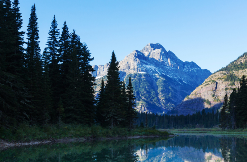 Dramatic cliffs and a calm lake within Glacier National Park on a clear day.