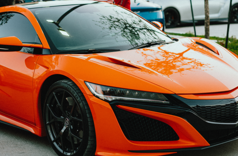 A sleek orange sports car sitting under the slight shadow of a tree.