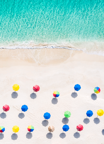 Colorful beach umbrellas scattered on a beach shore while the waves bubble.