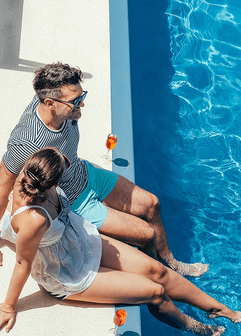 A man and woman enjoying their feet in a clear pool with drinks at their side