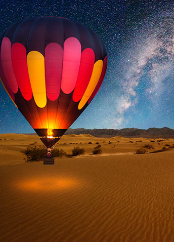 A hot air balloon afloat the desert in the night sky glittered with stars