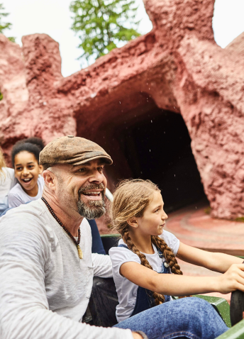 A family joyfully riding a roller coaster at Disneyland, with smiles and excitement on their faces.  