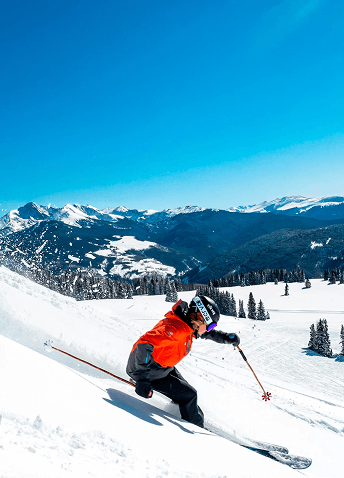 A person skiing down a snow mountain with a bright blue sky overhead.