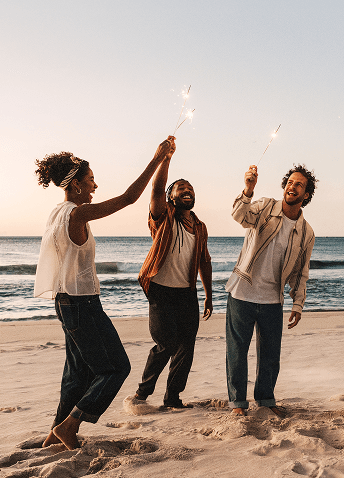 A group of people playing with sparklers at the beach during sunset.