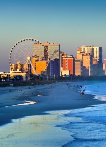 A skyline view of Myrtle Beach and its shores as the sun casts the buildings in gold.