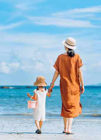 A mother and daughter holding hands while walking the sandy shores.