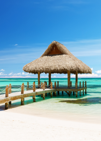 A view of a grass hut pier on a beach in crystal clear waters