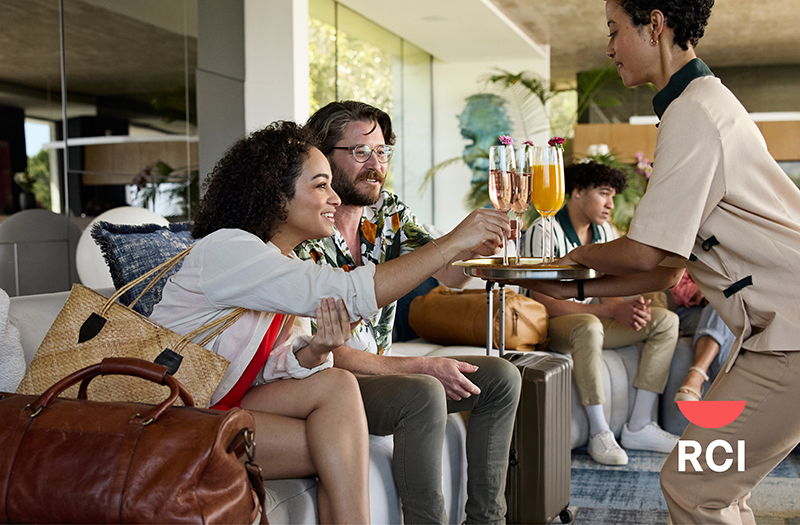 A resort staff member offering welcome drinks on a silver tray to a smiling couple seated in a luxury hotel lobby.