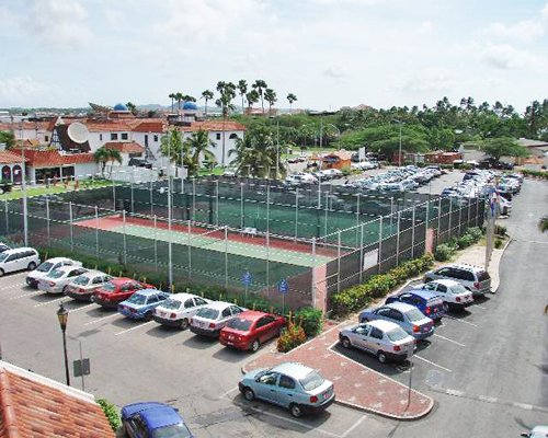 An aerial view of a fenced tennis court surrounded by a parking area.