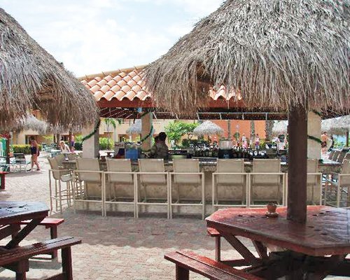 A poolside bar with hut along side thatched sunshades.