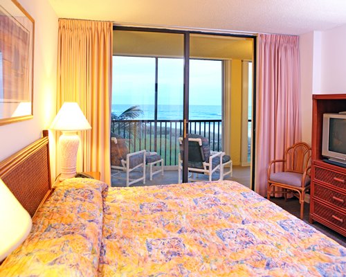 A view of well furnished bedroom with a king bed, television, and a balcony.