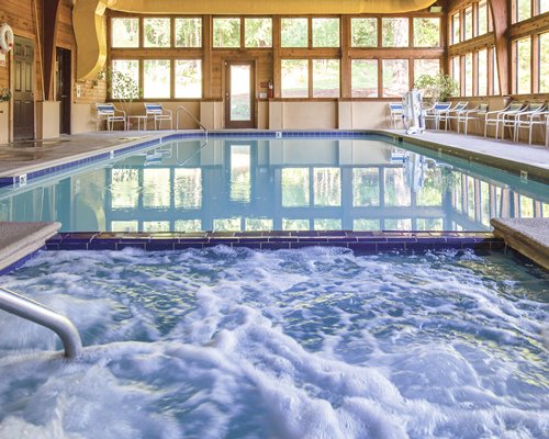 An indoor swimming pool and hot tub with patio chairs.