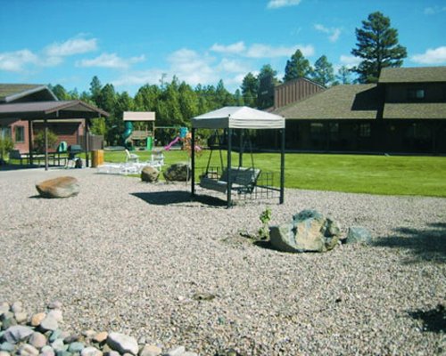 An outdoor picnic area with a swing alongside kids play ground surrounded by lawns.