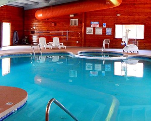 An indoor swimming pool with hot tub alongside lounge area.