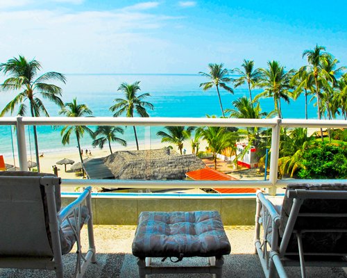 A balcony view of the ocean & beach surrounded by palm trees.