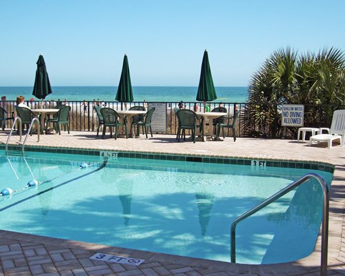An outdoor swimming pool with dining area alongside the ocean.