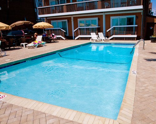 Outdoor pool with chaise lounge chairs and patio tables with umbrellas.