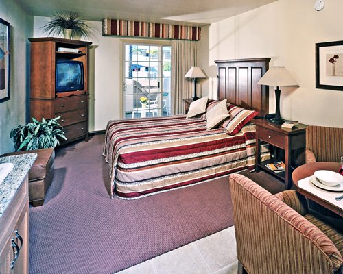 A well furnished bedroom with king bed television dining area and balcony with outdoor view.