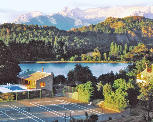 An outdoor tennis court alongside the lake surrounded by a wooded area.