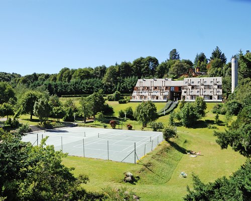 An outdoor tennis court alongside multi story units surrounded by wooded area.