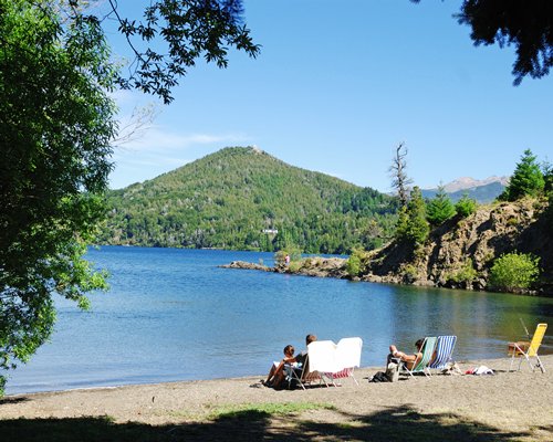 A view of the water in front of a hill surrounded by a wooded area.