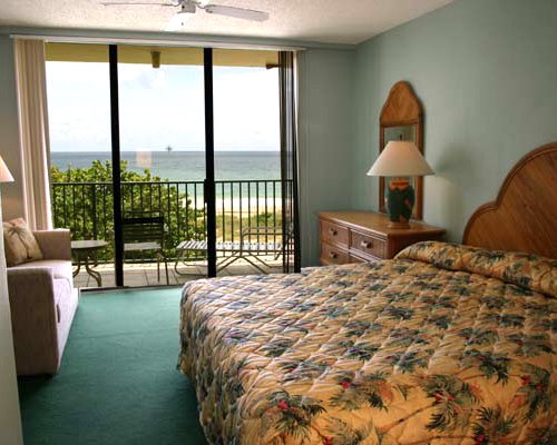 Furnished bedroom with king bed alongside a balcony with an ocean view.