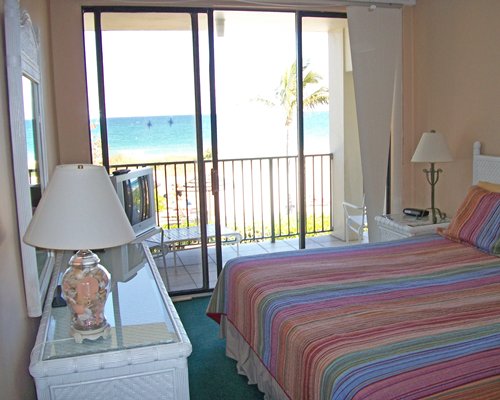 A furnished bedroom with television and a balcony supporting an ocean view.