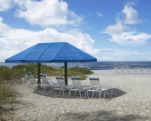 A beach view of chaise lounge chairs under a sunshade facing the ocean.