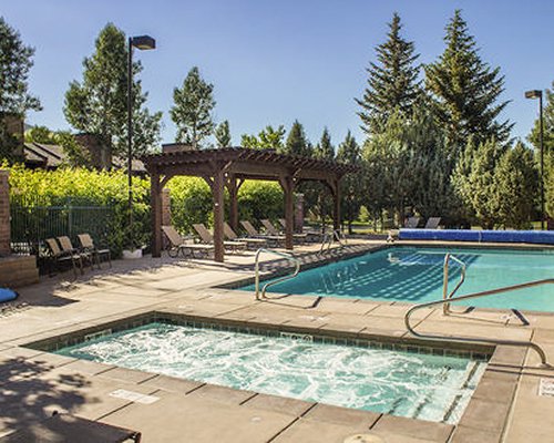 An outdoor swimming pool with hot tub surrounded by a wooded area.