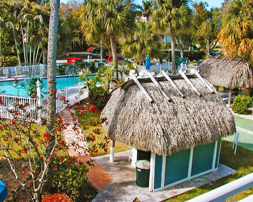 A scenic view of an outdoor swimming pool alongside thatched sunshades.