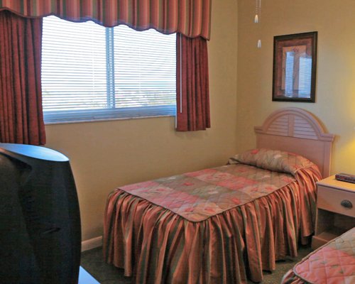 Furnished bedroom with twin beds television and outside view.