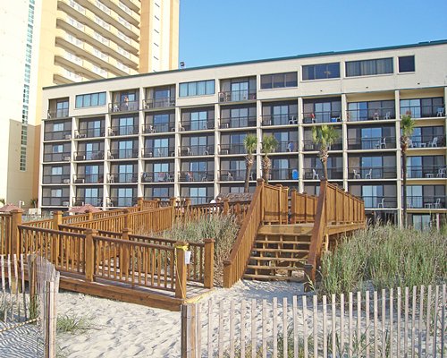 Exterior view of a multi story unit with private balconies behind a wooden pathway.