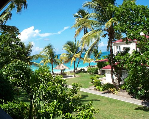 Scenic exterior view of a pathway to Antigua Village Beach Club and ocean with thatched sunshades.