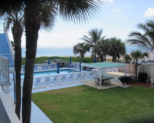 An outdoor swimming pool with chaise lounge chairs and thatched sunshade alongside resort.