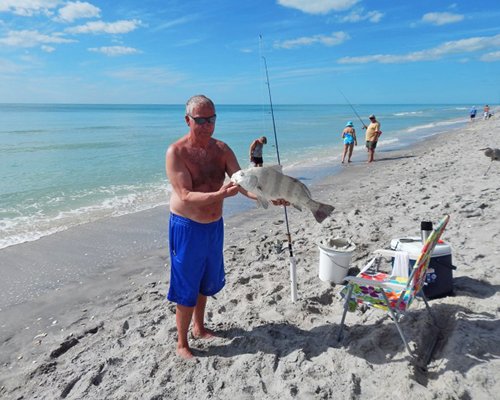 A man showing a fish he caught at the beach.
