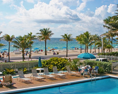 An outside swimming pool with chaise lounge chairs alongside ocean.
