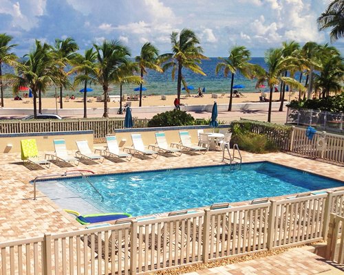 Outdoor swimming pool with chaise lounge chairs palm trees and ocean view.