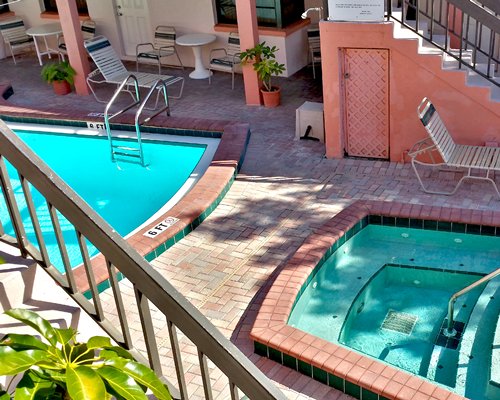 An outdoor swimming pool with chaise lounge chairs and a hot tub alongside resort units.