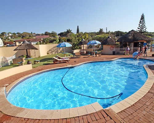 An outdoor swimming pool with chaise lounge chairs and thatched sunshades.